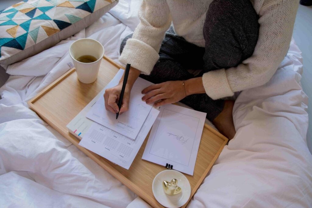 Vrouw zit op bed en schrijft in een schrift